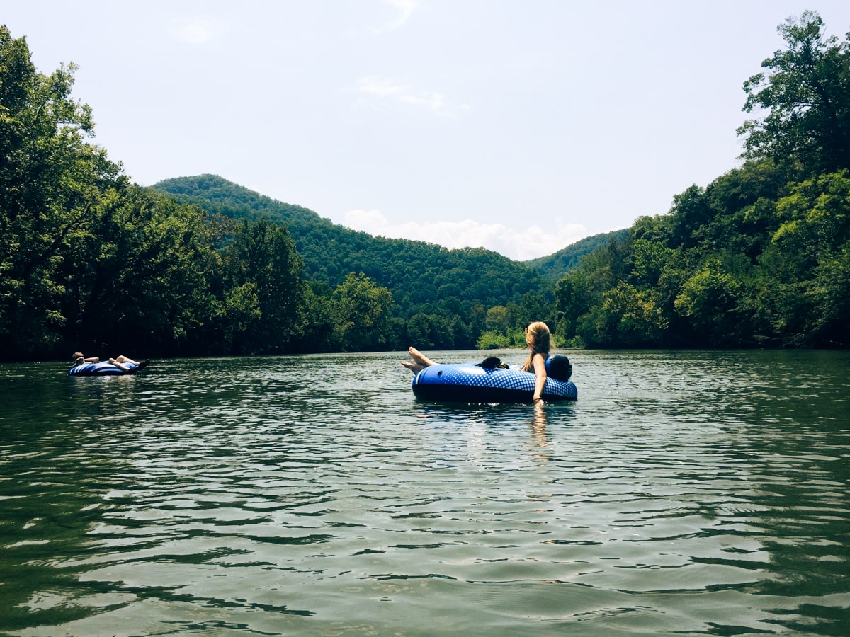 Girl floating down the river on an inner tube in the Nolichucky River with mountains in the background