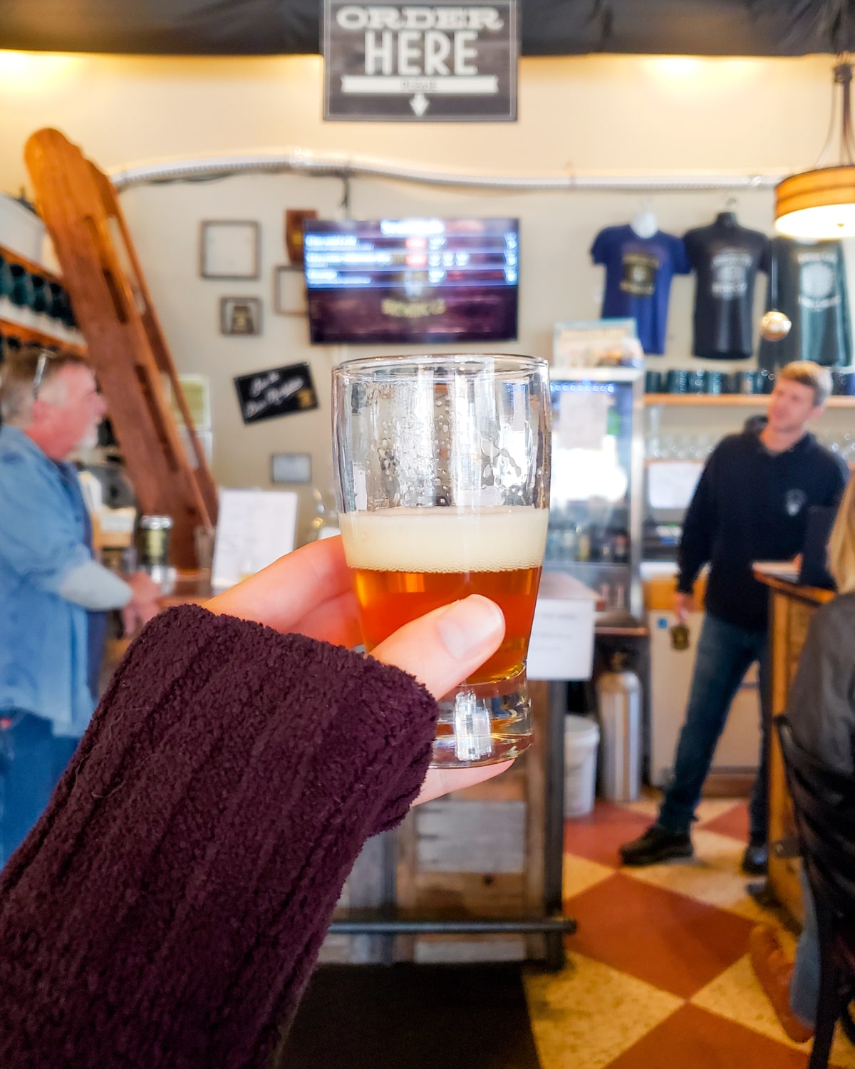 Woman holding craft beer up inside Johnson City Brewing Company with people and shop in background