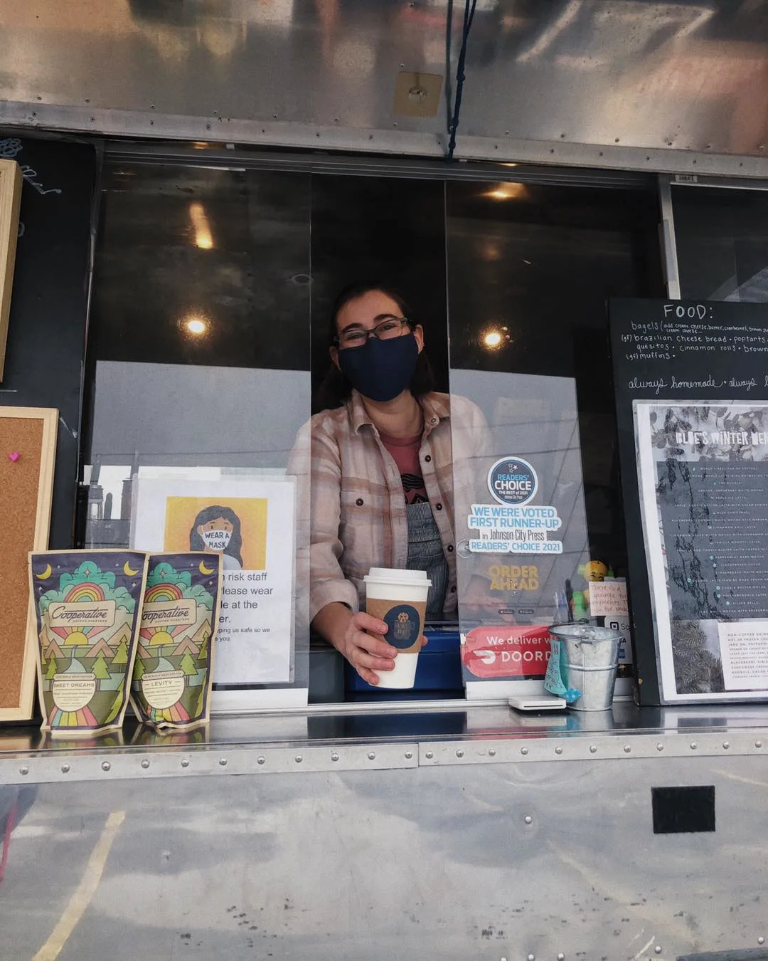 Barista at Blue's Brews airstream cafe serving coffee from window