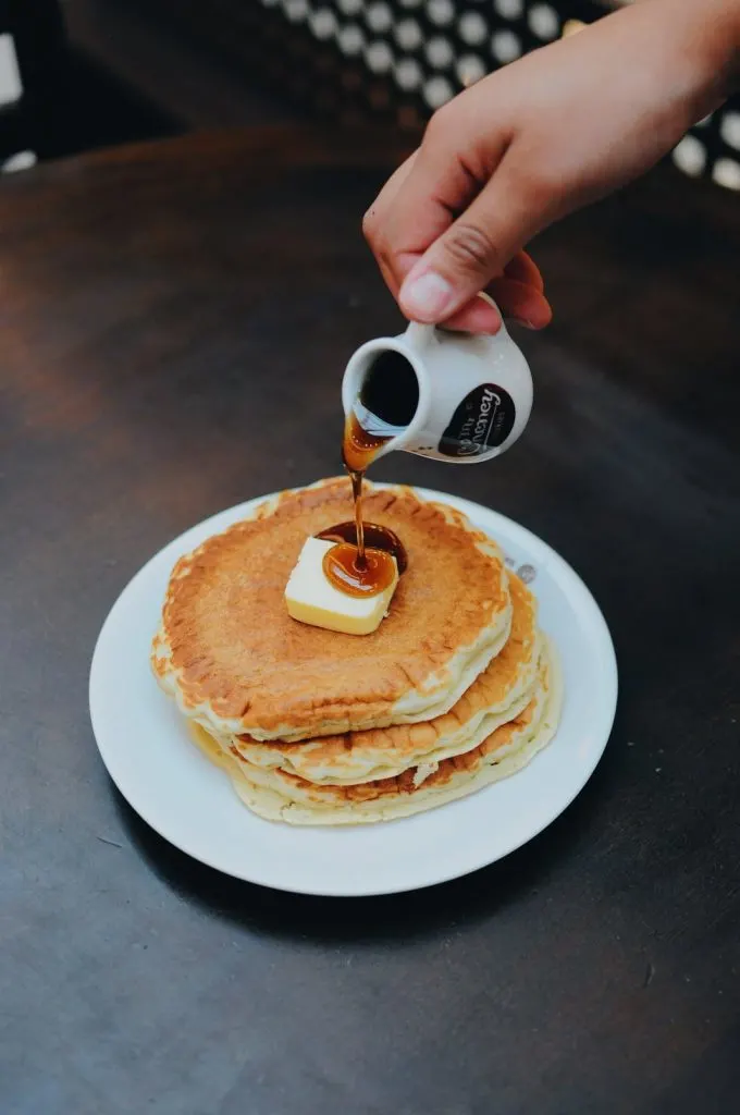 Person pouring maple syrup of stack of buttermilk pancakes