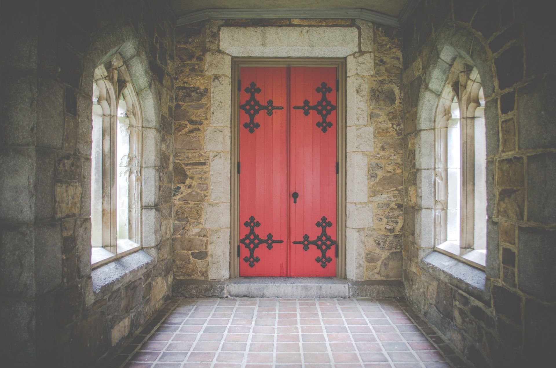 Stone walls and triangular windows with red ornate door inside church.