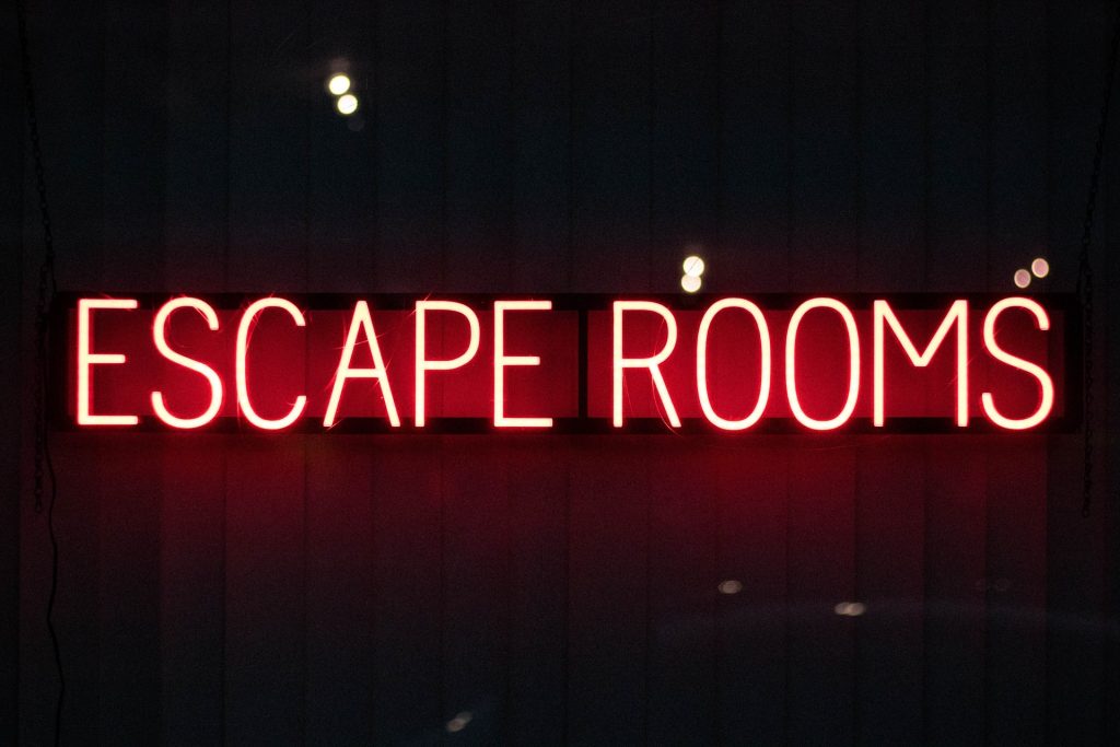 Neon red sign that says, "ESCAPE ROOMS" in dark room