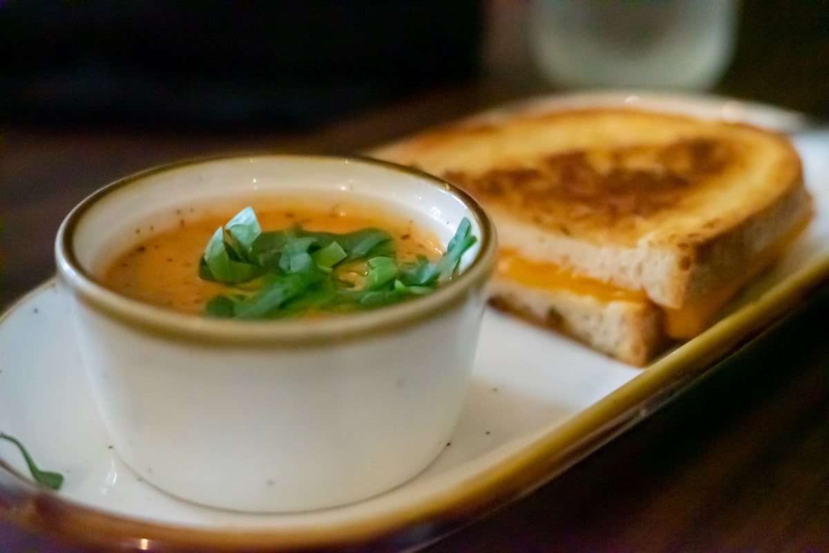 Bowl of tomato soup and half grilled cheese sandwich on plate.