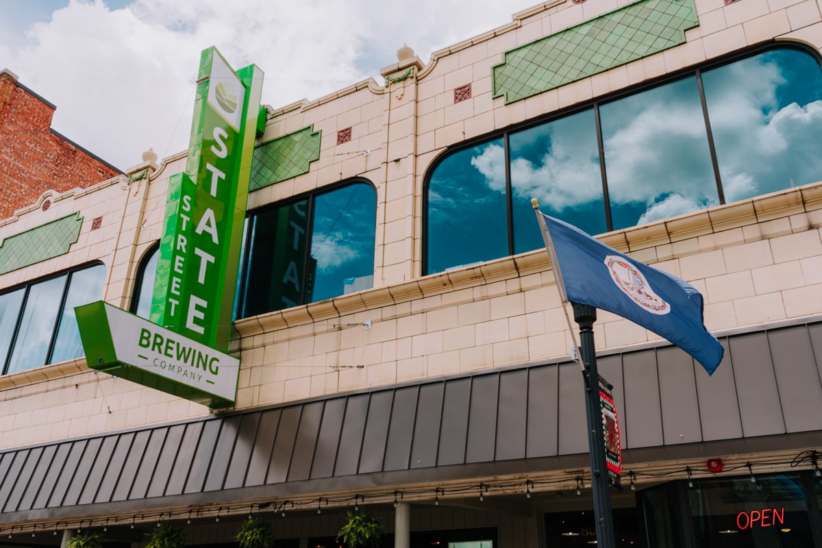 Green street sign of State Street Brewing with reflection of the blue sky in windows.