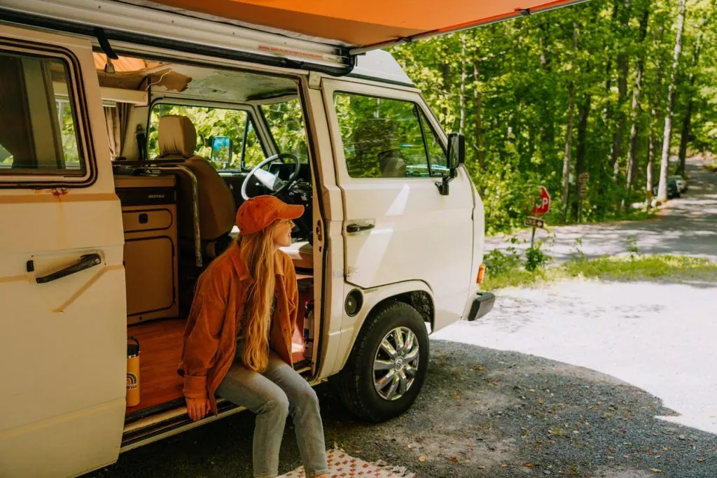 Woman wearing boho jacket and orange hat sitting on Westaflia van step at Cardens Bluff Campground in Watagua Lake Tennessee