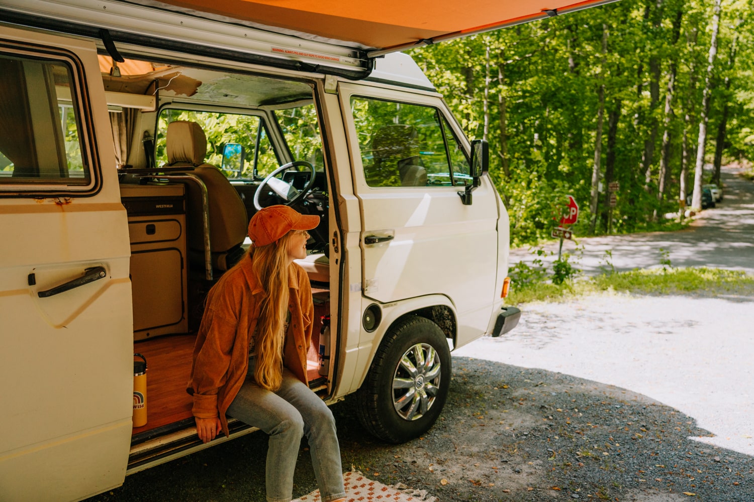 Woman wearing boho jacket and orange hat sitting on Westaflia van camper