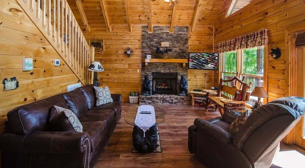 living room of a wood cabin with fireplace and leather couches.