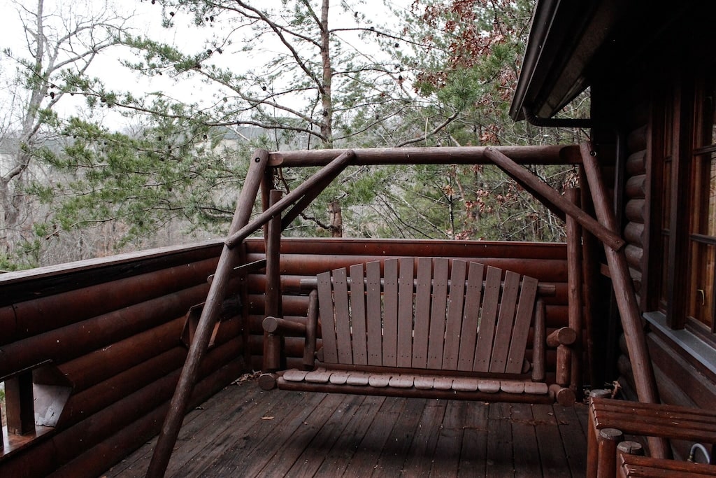 swinging chair on a log cabin porch with trees in the background