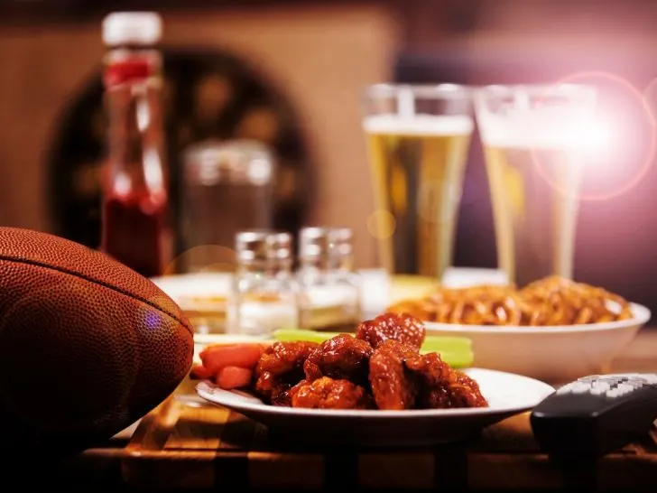 Plate of chicken wings and pub food, with football on table inside restaurant.