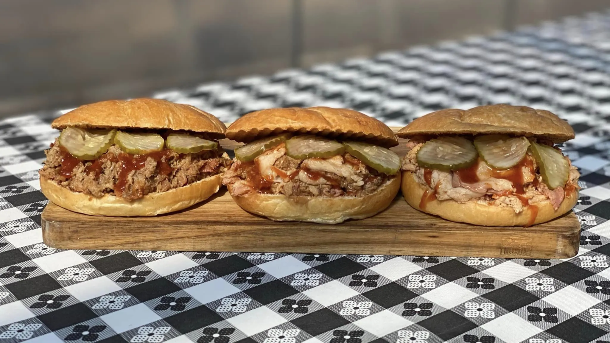 Three smoked chicken sandwiches on checkered black-n-white table cloth.