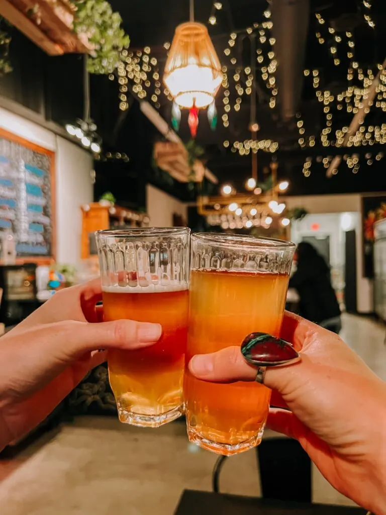 Two girls clinking golden beers together inside Blues Brews Beer Garden.