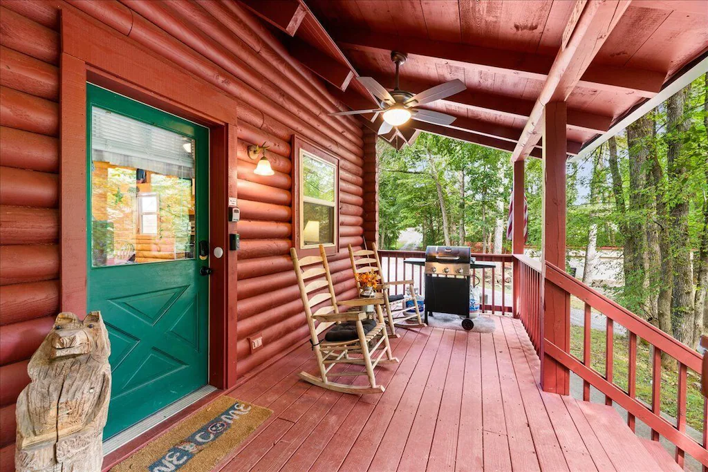 Red log cabin in Knoxville for rent with porch chairs and bbq grill.