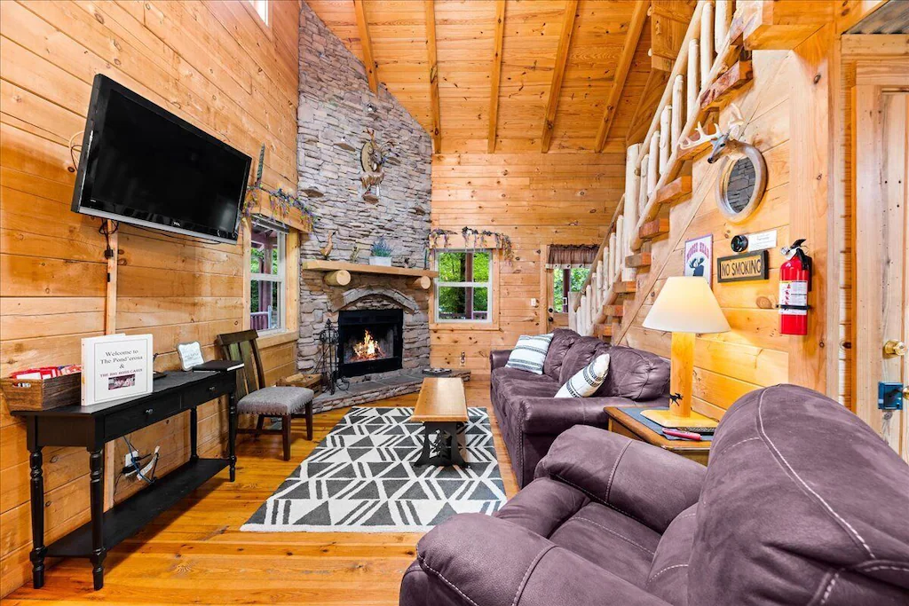 Inside a beautiful wooden cabin with plush sofa chairs, TV, and fireplace.