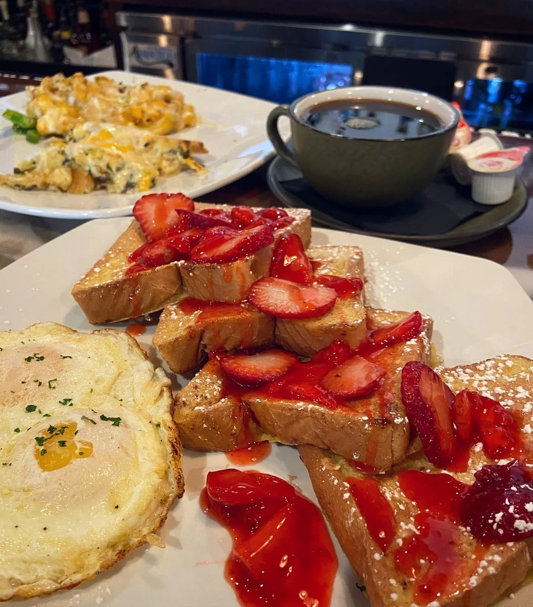 French toast topped with syrup, strawberries, and powered sugar with fried eggs