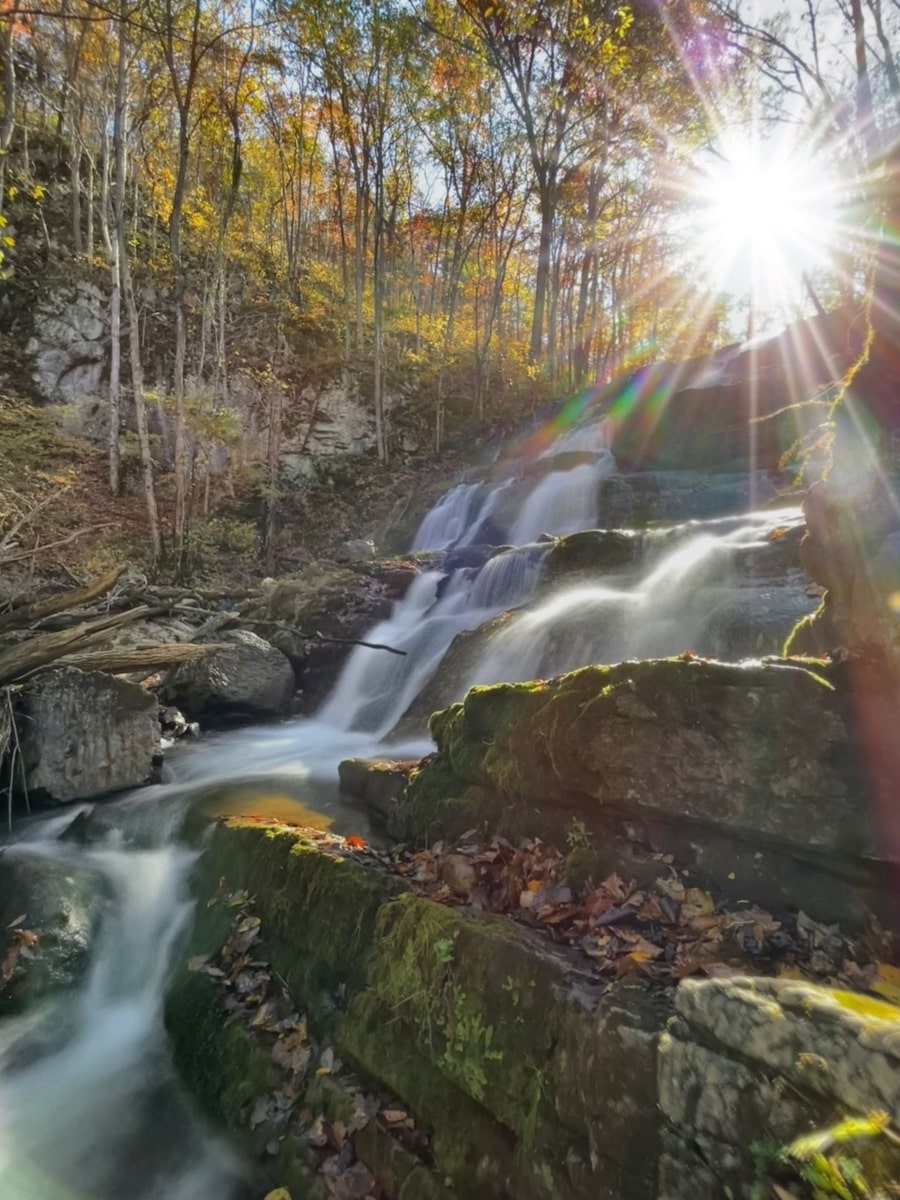 Logan Creek Falls cascading over rocks with the sun shining in the background