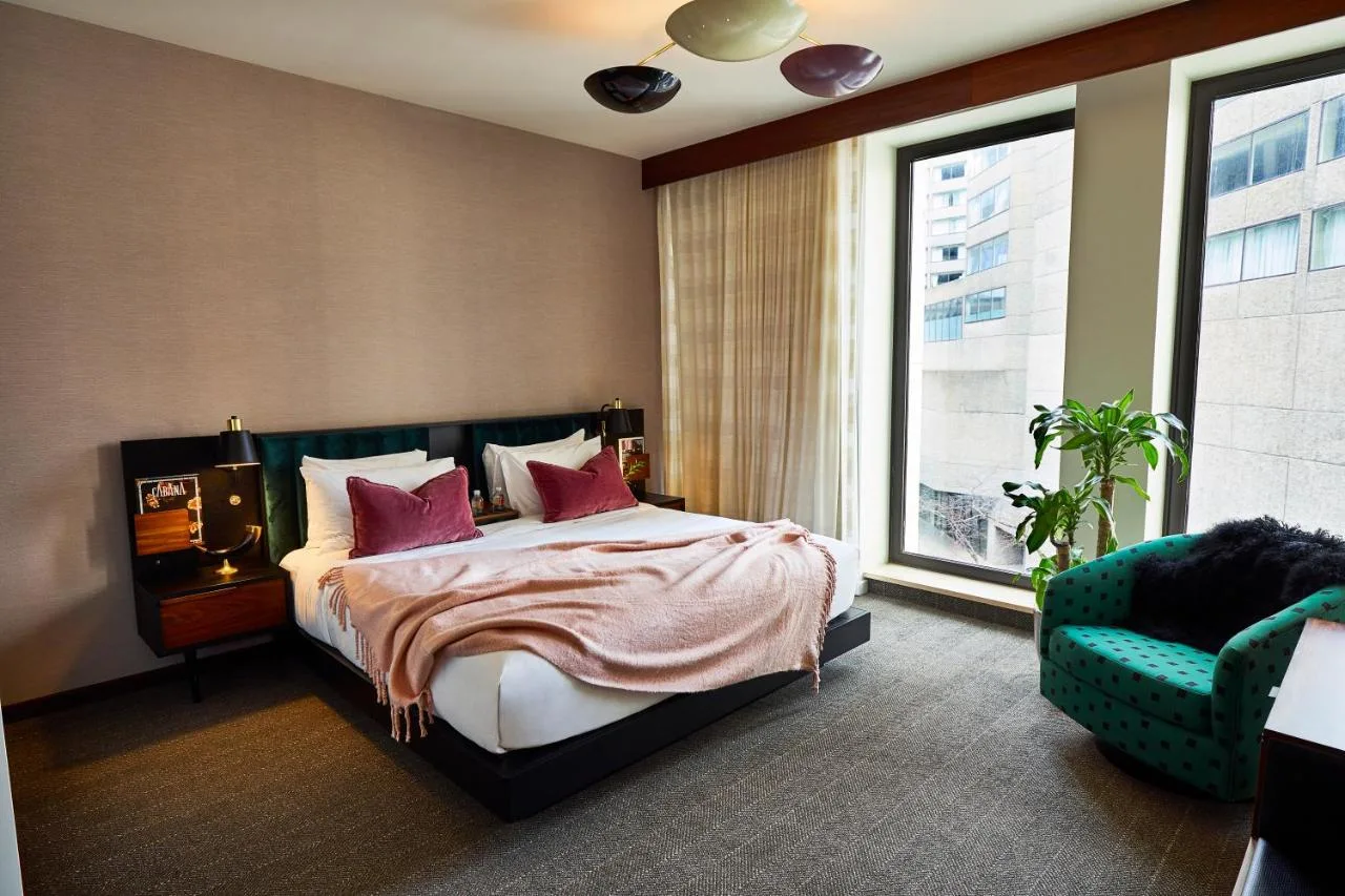 plush bed with blanket and velvet pillows with large windows and velvet chair at the fairlane hotel in nashville tn 