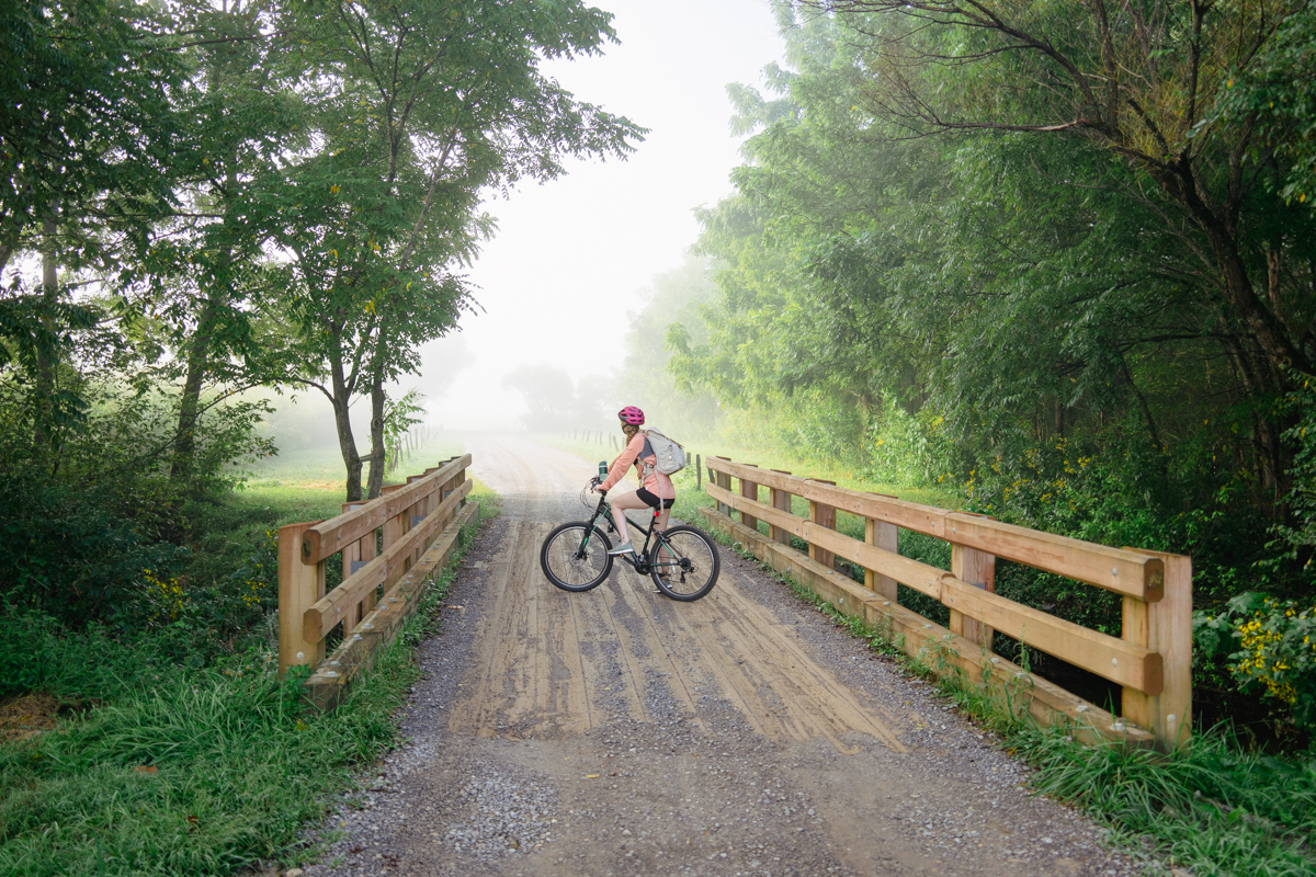 woman biking cades cove loop early in the morning on a gravel road with a pink helmet