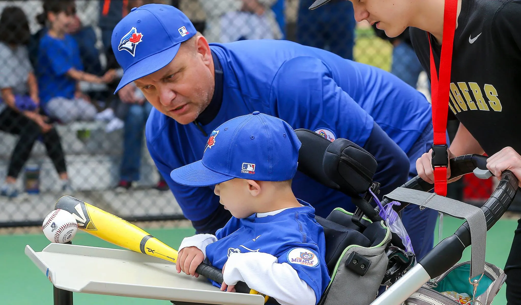 little boy in a wheelchair playing baseball with assistance from coach