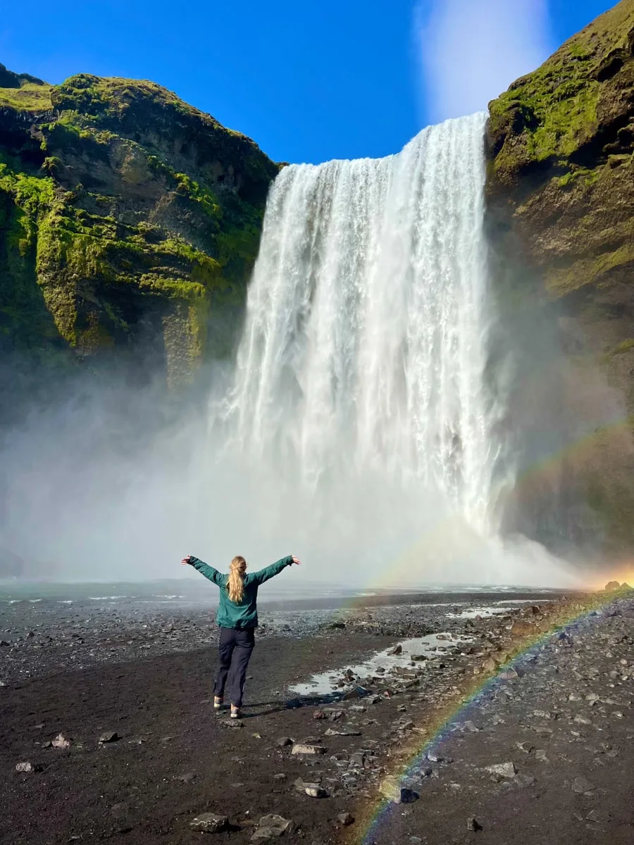 laurin standing in front of a large waterfall with rainbow in Iceland