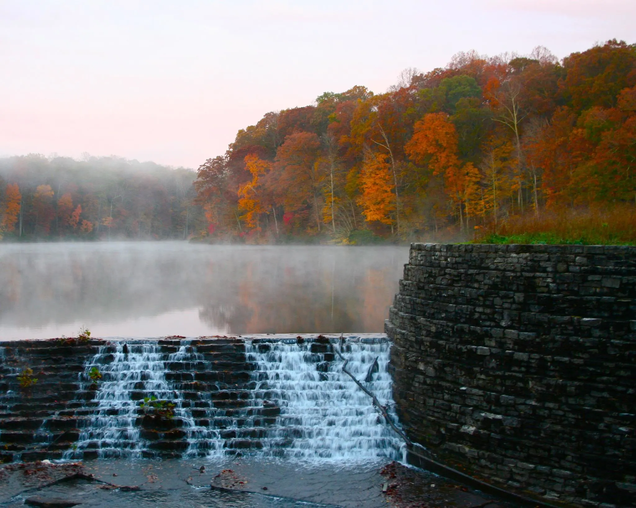 fog over the lake with fall foliage trees and water cascading down over steps at montgomery bell state park near nashville tn 