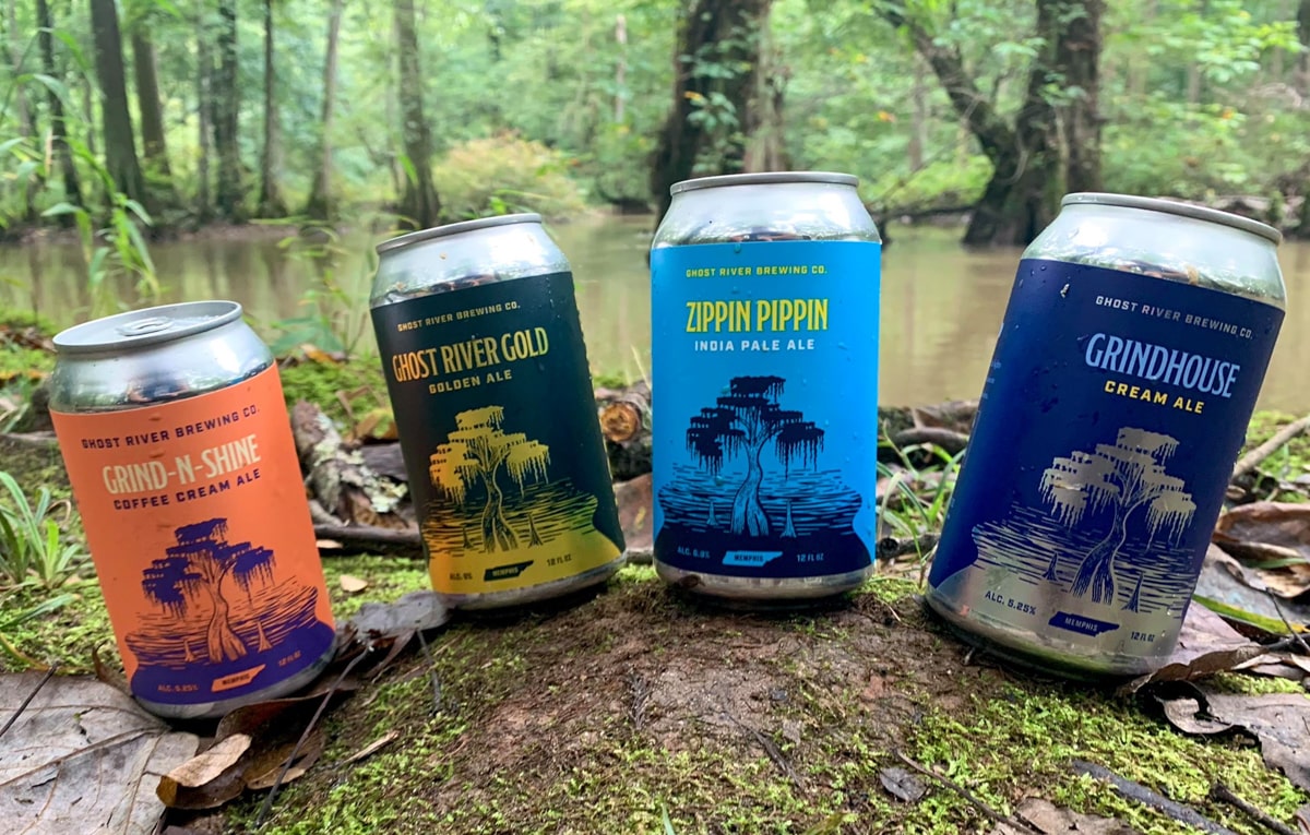 four cans of beer from ghost river brewing sitting on a rock with the river in the background in memphis