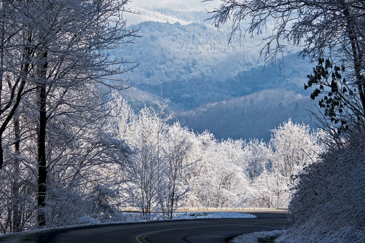 road leading down into the smoky mountains with snow on top of the trees and mountains in the background