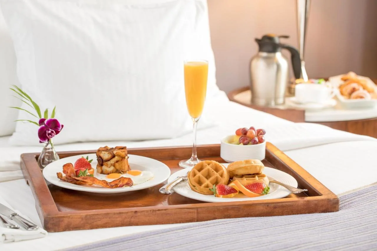 breakfast in bed tray with waffles and bacon and a mimosa on a made bed with white sheets at the peabody hotel in memphis