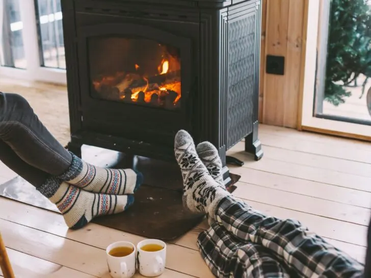 People sitting around a fireplace with cups of hot coffee in a cozy cabin